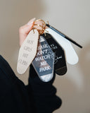 Hand holding assorted motel-style keychains including the Keys to the Shit Show Keychain