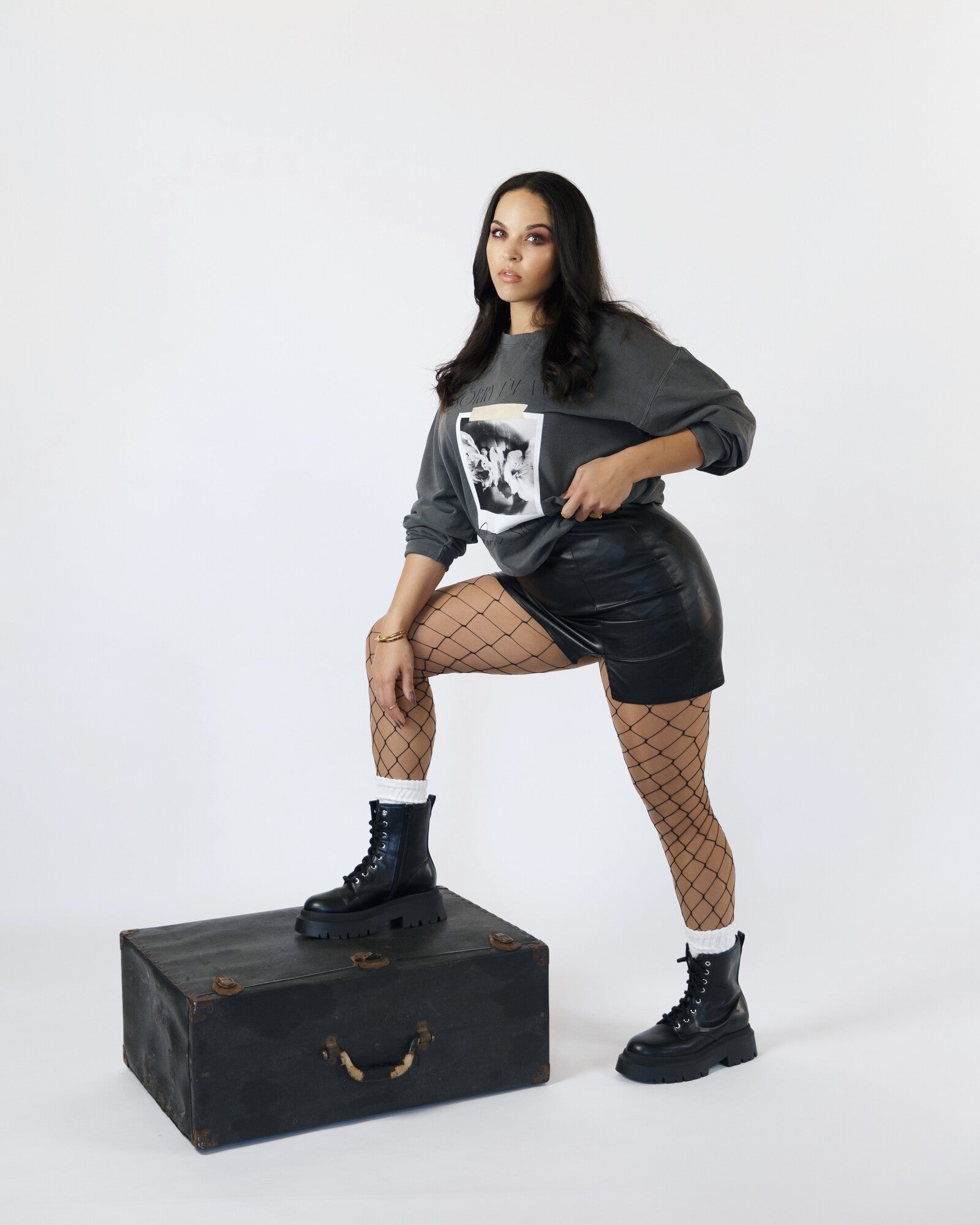 Model wearing the charcoal Earth Sign crewneck seated on a black case.