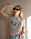 Model wearing the gray This Is a Big Inconvenience baby tee with sunglasses and red accessories.