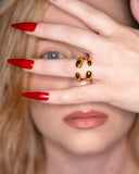 Atalanta open gold bypass ring worn with long red nails in a close face portrait.