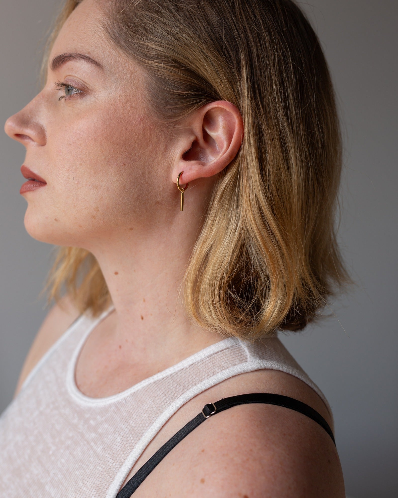 Ava gold bar drop earring worn in a clean side-profile portrait.