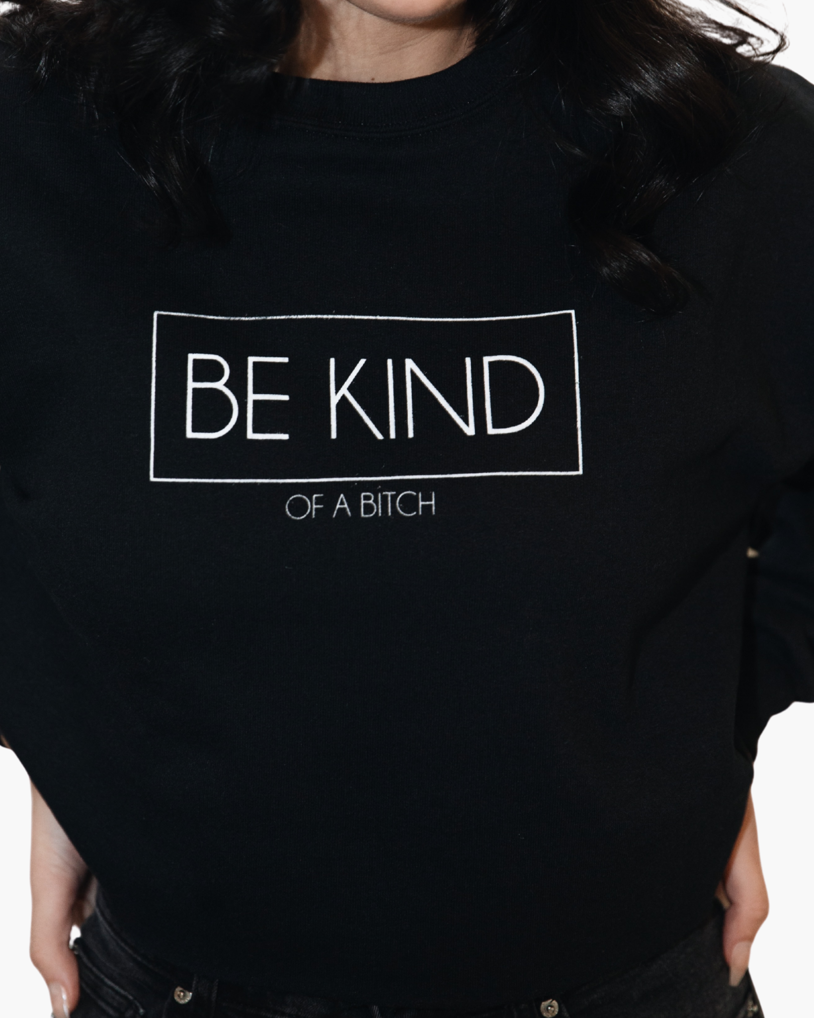 Black crewneck sweatshirt with white outlined text reading Be Kind and smaller text reading Of a Bitch.