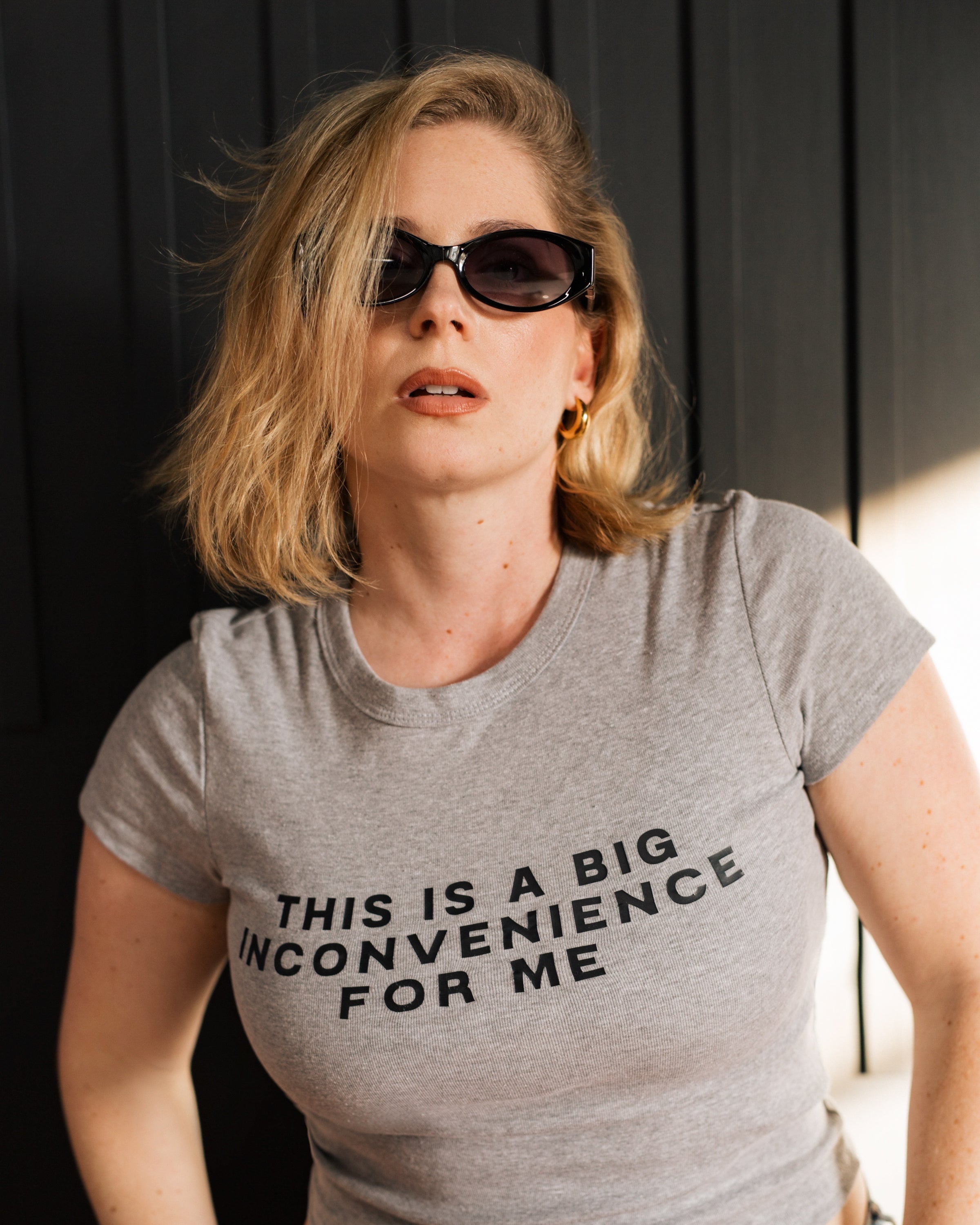 Model showing the fitted mid-length cut of the gray Big Inconvenience baby tee.