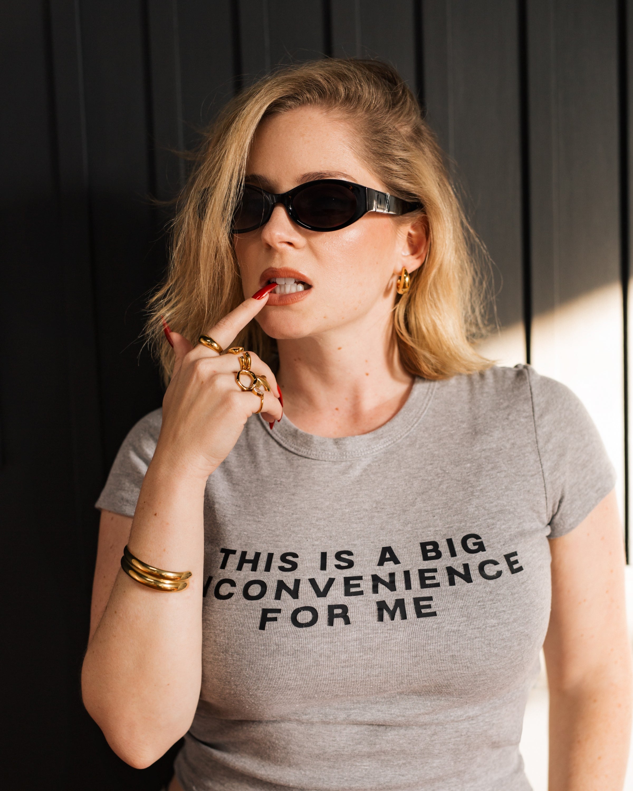 Model wearing the gray Big Inconvenience baby tee with black sunglasses in warm light.