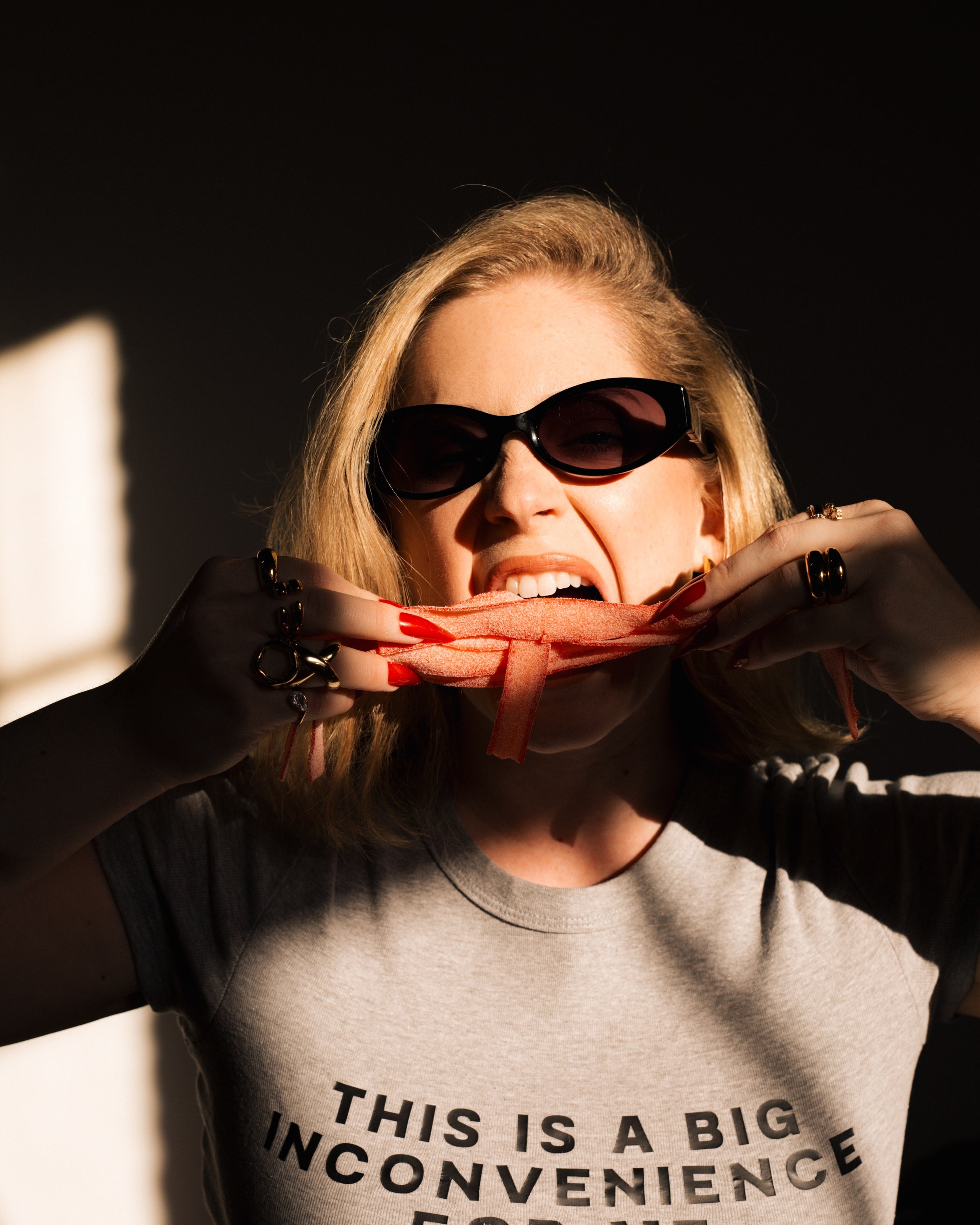 Model wearing the gray Big Inconvenience baby tee in a playful red ribbon styling shot.