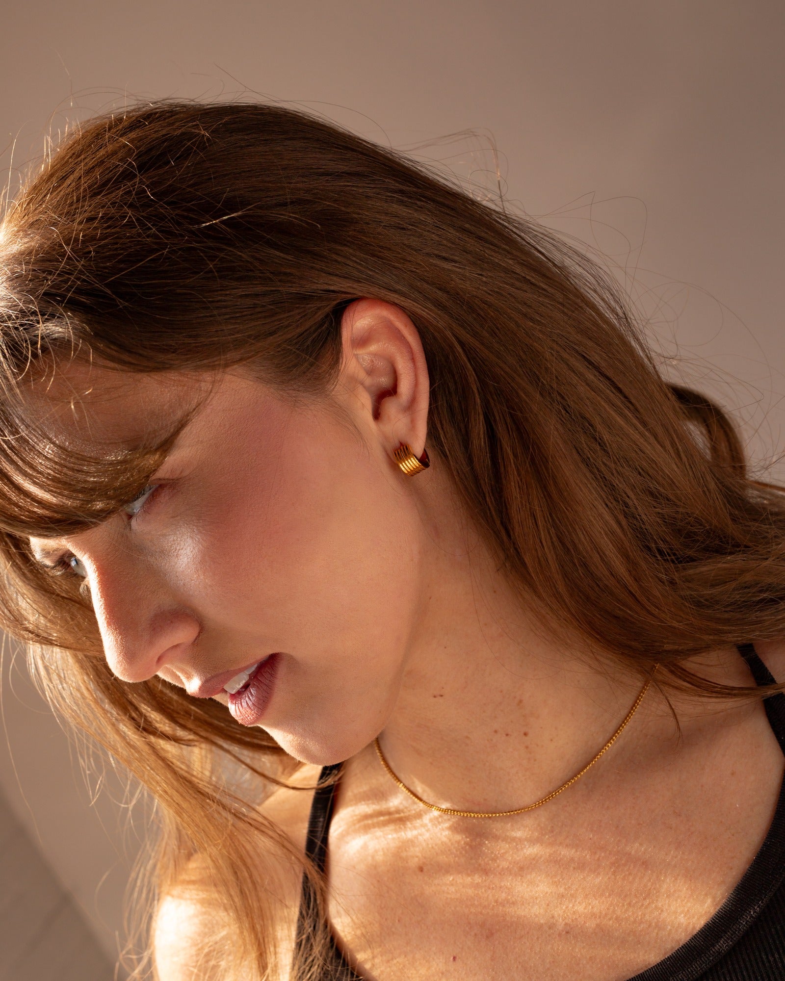 Cleo gold huggie worn in a warm light lifestyle portrait.