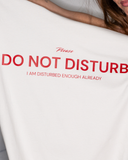 Bone-colored crewneck T-shirt with deep red text reading Please Do Not Disturb — I Am Disturbed Enough Already.
