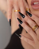 Euthenia textured gold band worn with stacked rings and long black nails in a close hand-to-face portrait.