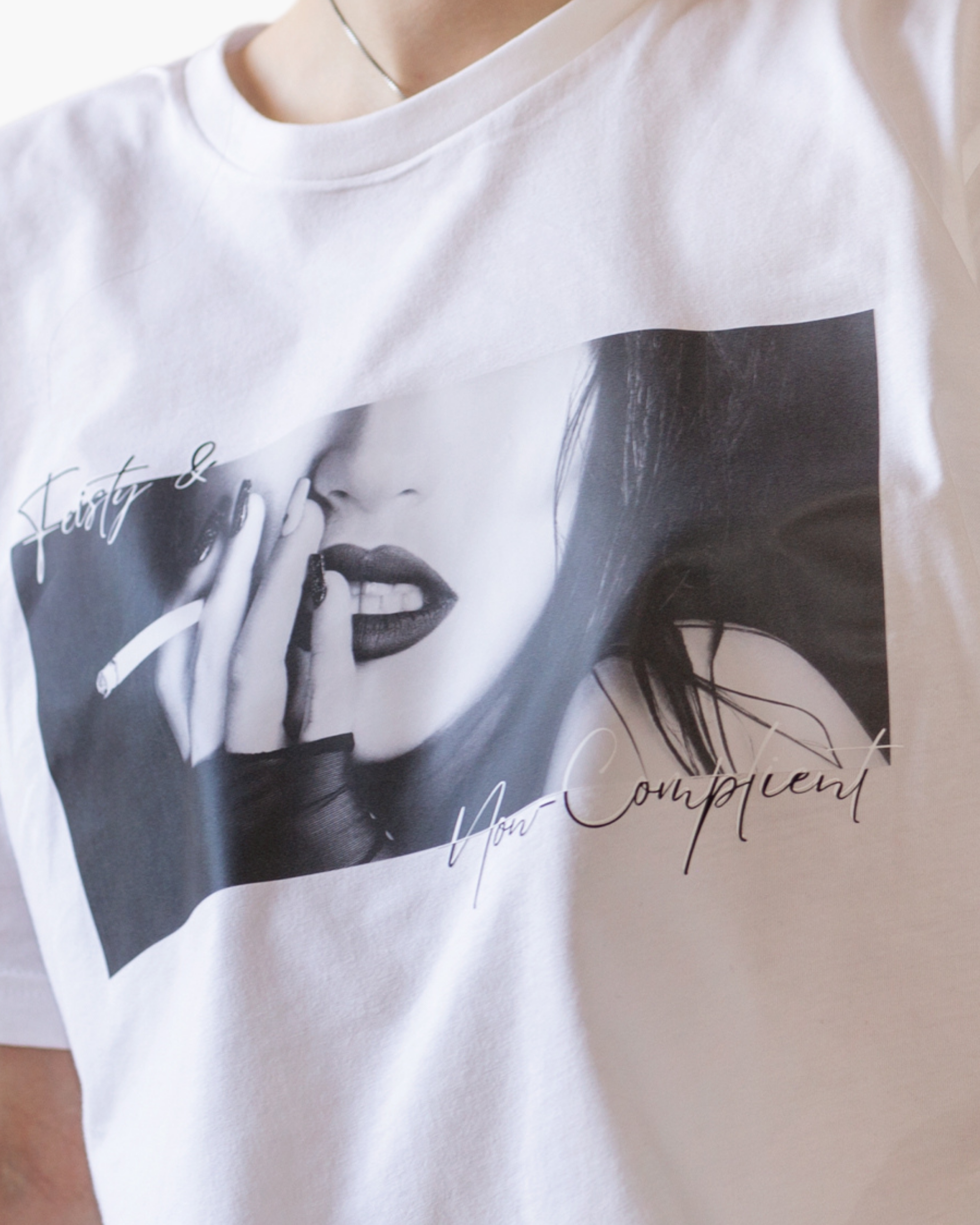 White crewneck T-shirt with a black-and-white editorial image and handwritten Feisty & Non-Compliant text.