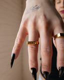Fuck Off engraved gold ring worn with long black nails in a close hand detail.