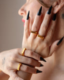 Fuck Off gold signet ring styled with black nails and stacked rings in a portrait.