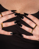 Fuck Off engraved ring worn with multiple gold rings and black nails.