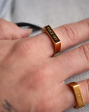Fuck Off gold signet ring shown in a tight hand detail with polished gold bands.