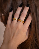 Harmonia watchband-link gold ring worn with long black nails in a close hand-to-face portrait.