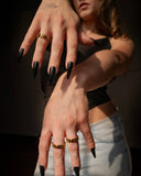 Harmonia polished gold link ring styled with layered rings and long black nails in a two-hand portrait.
