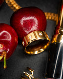 Jones gold triple-stone band styled with red apples, gold jewelry and a black lipstick tube.