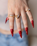 Liza rectangular clear-stone band styled with sculptural gold rings and long red nails.
