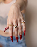 Liza gold eternity band shown in a relaxed hand portrait with clear-stone rings and red nails.