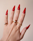Liza clear-stone eternity band styled with layered gold rings on an upright hand with red nails.
