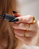 Manto black pear-stone wave ring worn with long black nails while holding a mascara wand.