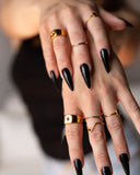 Manto gold wave ring styled with layered gold rings and long black nails in a close hand detail.