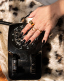 Manto black-stone wave ring worn with layered rings while resting a hand on a vintage rotary phone.