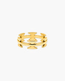 Polished gold-tone Nemesis ring with overlapping angular cutouts forming a bold zigzag geometric design on a white background.