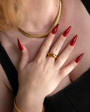 Octavia wide gold dome ring worn with long red nails in a close hand-at-chest portrait.
