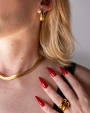 Octavia chunky gold band worn with long red nails in a close hand-to-neck portrait.