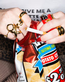 Octavia polished wide gold ring worn with mixed rings and long red nails while holding a snack bag.
