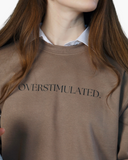 Warm brown crewneck sweatshirt with black text reading overstimulated.