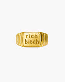 Polished gold-tone ribbed signet ring engraved with “rich bitch” on a white background.
