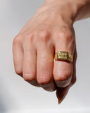 Rich Bitch gold signet ring worn in a tight fist and hand detail.