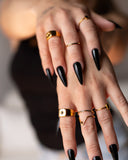 Summer gold signet ring styled with layered rings and long black nails in a two-hand detail.