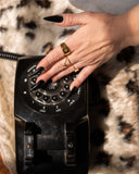Summer starburst ring worn with layered gold rings while resting a hand on a vintage rotary phone.