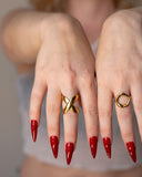X sculptural crossover ring worn with long red nails in a close hand portrait.