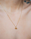 Close-up of a gold zodiac pendant necklace worn at the neckline.
